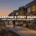 Twilight waterfront view of Kettlestone Lakes in Waukee with modern mixed-use buildings, outdoor dining, pedestrians, landscaped walkways, and a lively lifestyle-focused commercial district.