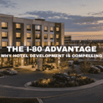 Modern hotel at Kettlestone Lakes in Waukee, Iowa with warm evening lighting, lakefront views, landscaped parking, walking paths, and nearby mixed-use commercial buildings.